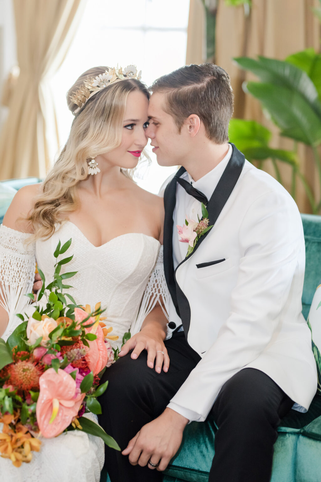 Florida Bride Wearing Vintage Strapless Sweetheart Neckline and Fringe Off the Shoulder Sleeve and Gold, Ivory Crown, Holding Tropical Pink Anthurium, Greenery, Pink Pin Cushion Protea Floral Bouquet and Groom Wearing White and Black Collar Tuxedo on Velvet Turquoise Couch | Wedding Hair and Makeup Adore Bridal Hair and Makeup