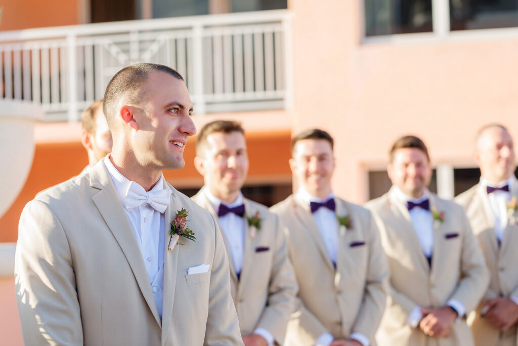 Florida Groom Happy Reaction to Bride Walking Down the Wedding Ceremony Aisle Wearing Tan Suit, White Bowtie and Pink Ginger Flower Boutonniere | Tampa Bay Wedding Photographer Limelight Photography