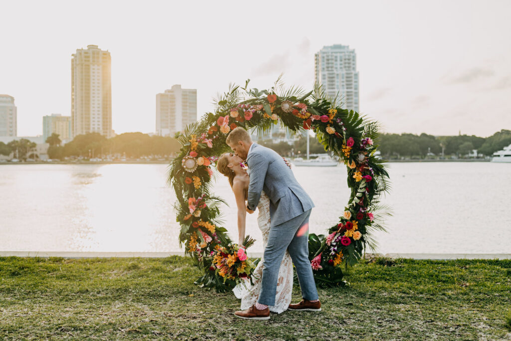 Bride and Groom Dip Kiss, Waterfront Tropical Wedding Ceremony Decor, Circular Colorful Floral Arch | Tampa Bay Wedding Photographer Amber McWhorter Photography
