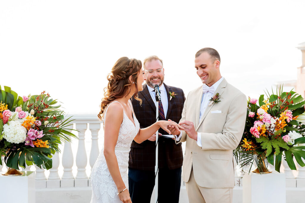 Florida Bride and Groom Exchanging Wedding Vows at Tropical Waterfront Rooftop Wedding Ceremony Hyatt Regency Clearwater Beach | Palm Fronds, Monstera Leaves, White Hydrangeas, Pink Ginger, Purple Orchids and Yellow Floral Arrangements on White Pedestals | Tampa Bay Wedding Photographer Limelight Photography