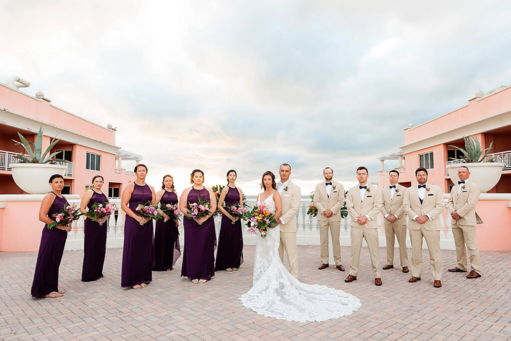 Florida Bride, Groom and Wedding Party | Bridesmaids in Matching Halter Purple Dresses Holding Tropical Floral Bouquets, Groomsmen in Tan Suits | Rooftop Waterfront Wedding Ceremony Venue Hyatt Regency Clearwater Beach | Tampa Bay Wedding Photographer Limelight Photography