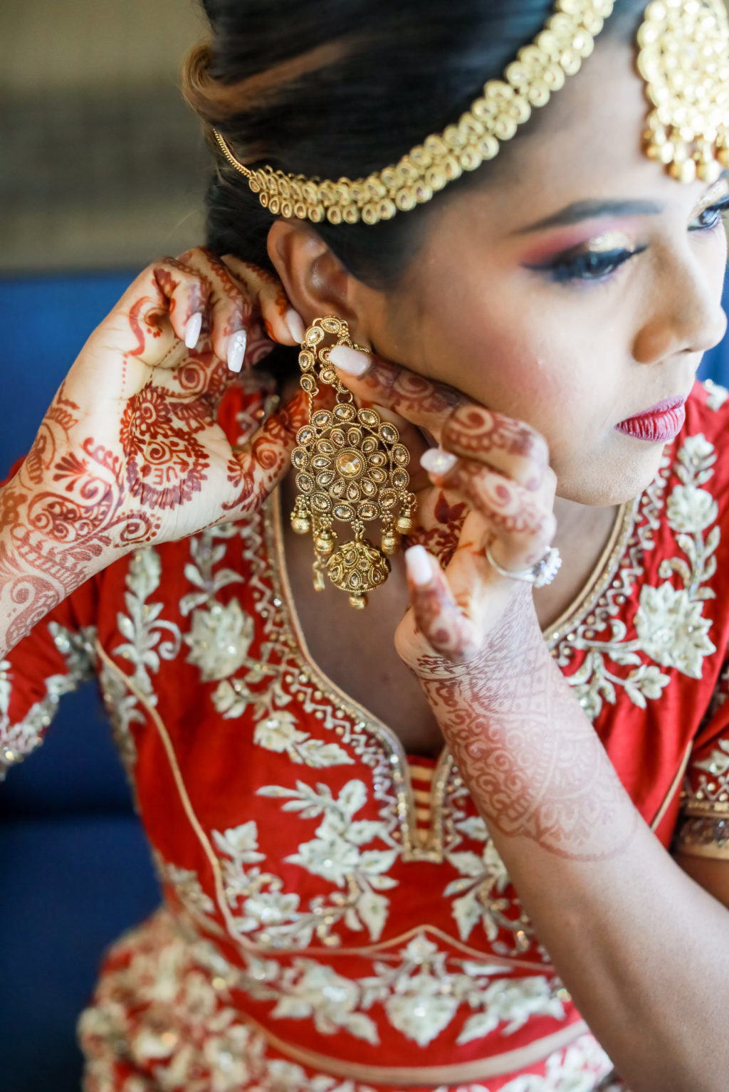 Hindu Indian Bride Getting Wedding Ready Putting on Elaborate Gold Dangle Earrings and Gold Headpiece | Tampa Bay Wedding Photographer Lifelong Photography Studios