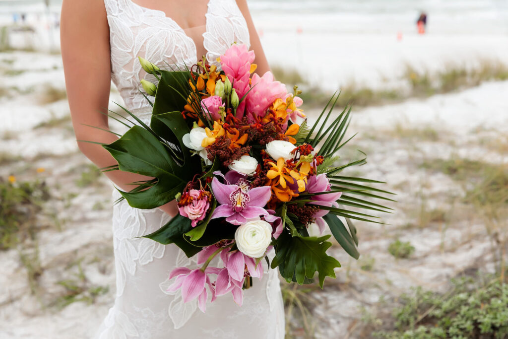 Clearwater Beach Bride Standing in Sand Wearing Romantic Floral Lace and Illusion Wedding Dress Holding Tropical Floral Bouquet Monstera Leaves, Palm Fronds, Pink Ginger, Purple Orchids, White Roses Floral Bouquet | Tampa Bay Wedding Photographer Limelight Photography