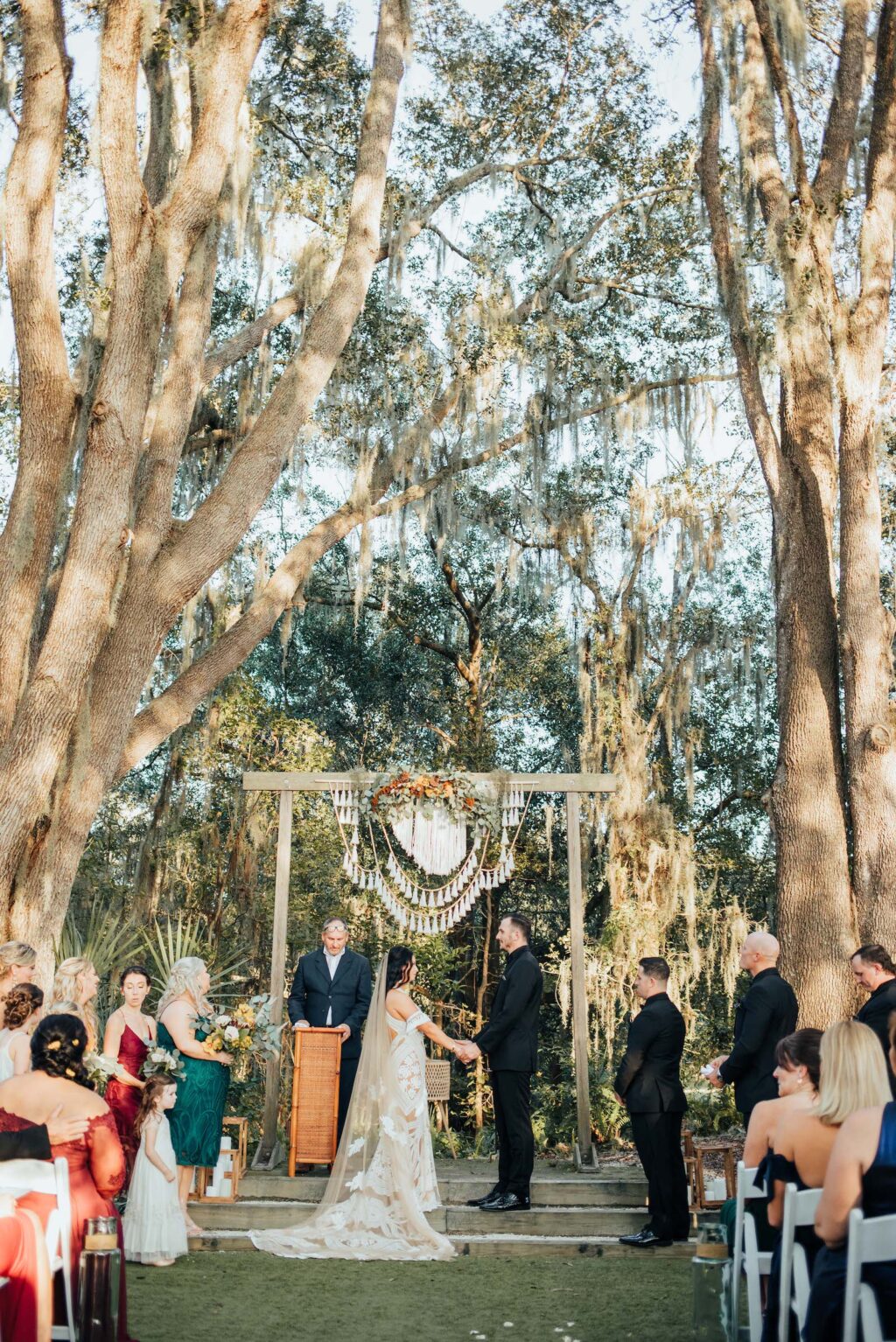 Bride and Groom Exchange Vows | Outdoor Bohemian Wedding Ceremony with White Garden Chairs | Wooden Arch with Crochet Details | Tampa Wedding Venue Paradise Springs