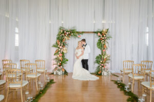Bride and Groom Under Tropical Elegant Wedding Ceremony Decor, Tropical Arch with Palm Fronts, Gold Painted Monstera Leaves, Pink Ginger, Pink Anthuriums and Orange Flowers, Floating Candles, Gold Vintage Chairs, White Linen Draping Backdrop | Tampa Bay Wedding Planner Eventfull Weddings | Wedding Linen Rentals Gabro Event Services | Wedding Chair Rentals A Chair Affair