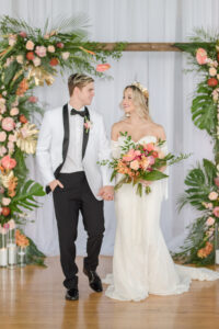 Bride and Groom Under Tropical Elegant Wedding Ceremony Decor, Tropical Arch with Palm Fronts, Gold Painted Monstera Leaves, Pink Ginger, Pink Anthuriums and Orange Flowers, Floating Candles, Gold Vintage Chairs, White Linen Draping Backdrop | Tampa Bay Wedding Planner Eventfull Weddings | Wedding Linen Rentals Gabro Event Services | Wedding Chair Rentals A Chair Affair | Adore Bridal Hair and Makeup