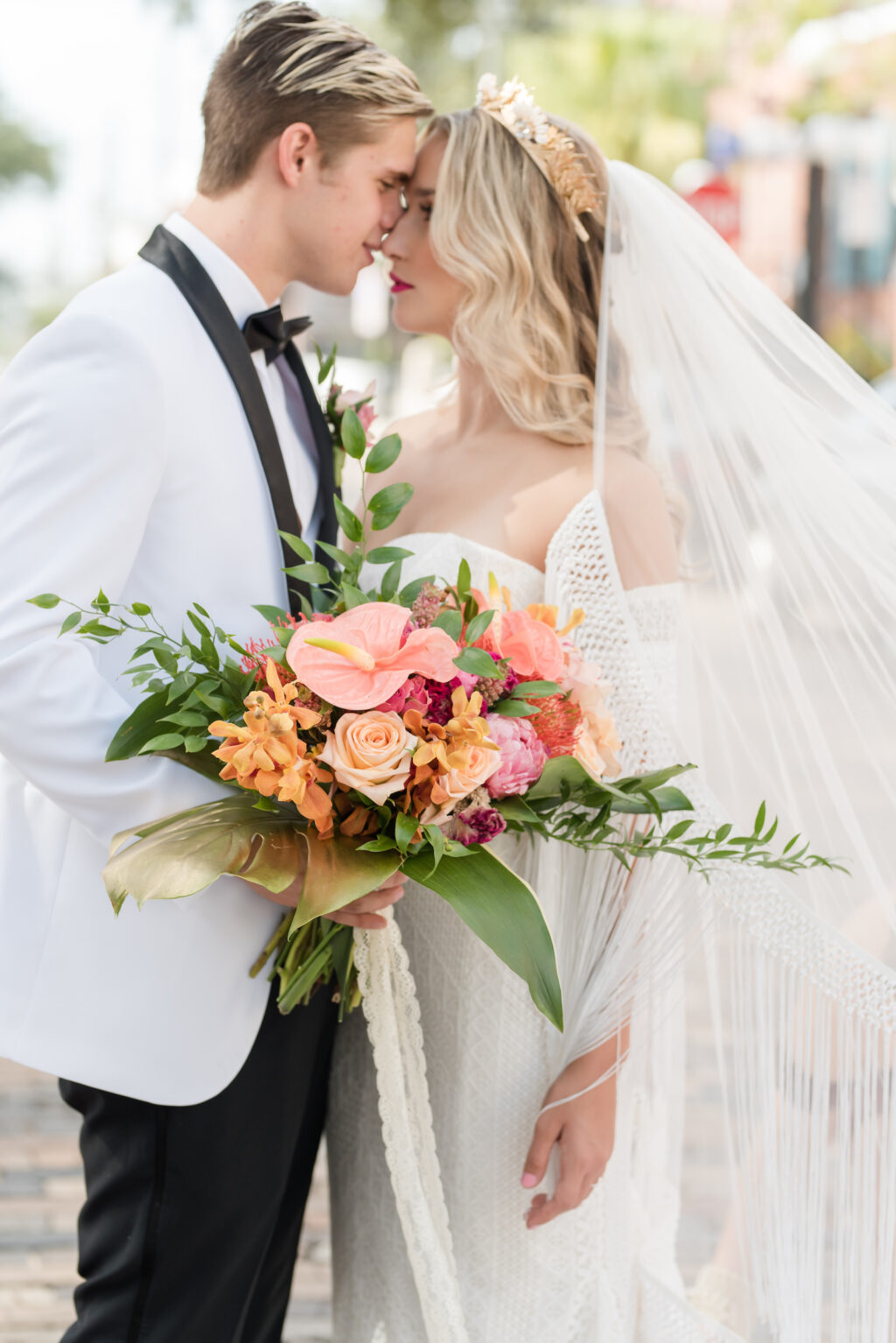 Vintage Bride Wearing Lace Strapless Sweetheart Neckline Fringe Off the Shoulder Sleeve Wedding Dress with Train, Gold Flower Crown Holding Colorful Tropical Floral Bouquet with Groom in White and Black Collar Tuxedo Standing in Streets of Tampa | Wedding Hair and Makeup Adore Bridal Hair and Makeup