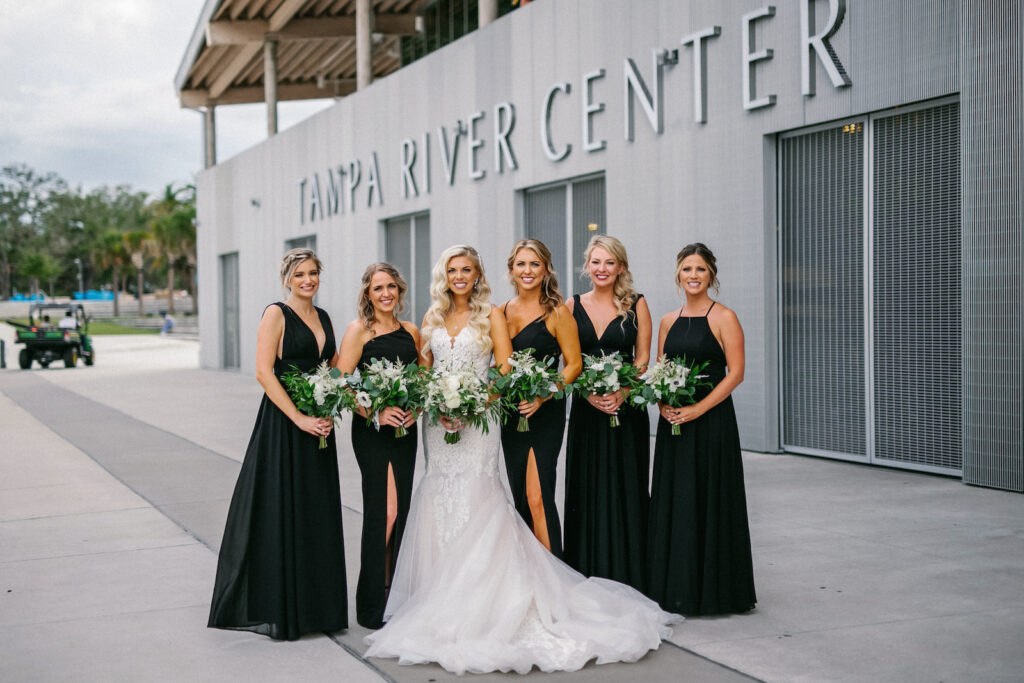 Modern Elegant Florida Bride Wearing Romantic Lace and Tulle Skirt Mermaid Wedding Dress and Bridesmaids in Mix and Match Black Dresses Outside Wedding Venue Tampa River Center