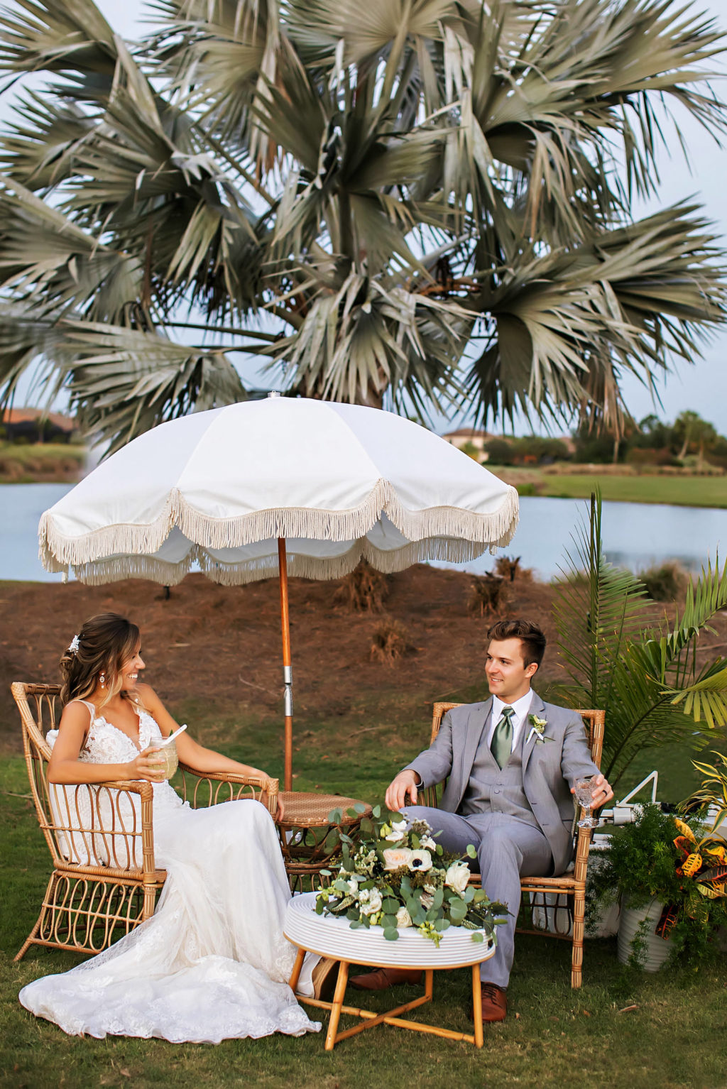 Florida Bride and Groom Sitting Outside During Wedding Reception on Bamboo Lounge Chairs, White Umbrella, Greenery and White Anemone Floral Bouquet | Tampa Bay Wedding Photographer Limelight Photography | Wedding Planner MDP Events | Wedding Dress Truly Forever Bridal Sarasota | Wedding Venue Esplanade Country Club | Wedding Florist Beneva Florals | Styled Shoot