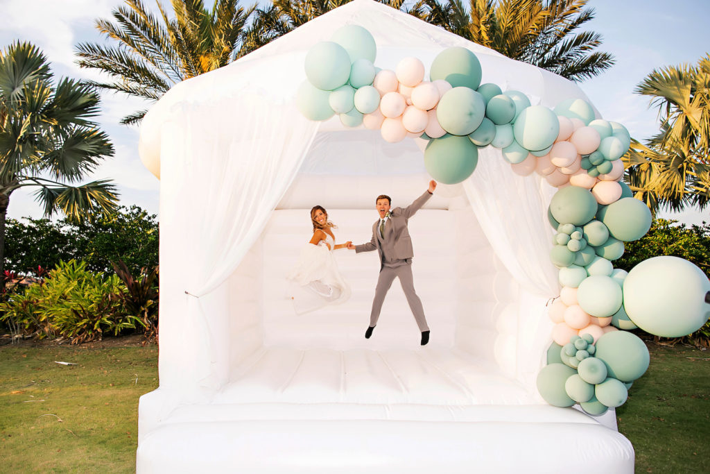 Bride and Groom Jumping on Fun, Unique White Adult Bounce House, Sage Green and Peach Balloons | Tampa Bay Wedding Photographer Limelight Photography | Wedding Planner MDP Events | Wedding Venue Esplanade Country Club | Styled Shoot