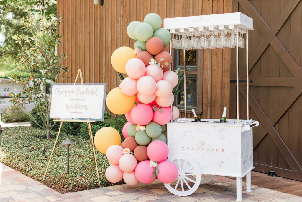 White Champagne Cart with Pink, Blush, Yellow, Sage Green and Terracotta Balloon Garland, White and Gold Acrylic Sign by Kruga | Sweet Bakehouse and Balloons | Prop Champagne Decor and Rentals | Florida Wedding Venue Mision Lago Estates | Big Fake Wedding