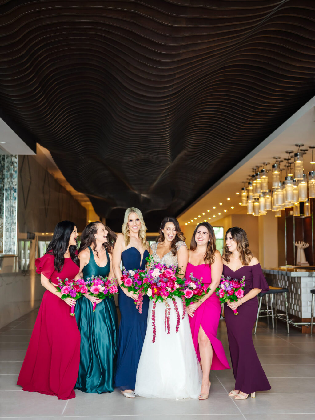 Bride Wearing Gold and Silver Beaded Cap Sleeve Bodice and Flowy Sheath Skirt Wedding Dress Holding Colorful Pink, Purple, Blush Pink, Greenery and Hanging Amaranthus Floral Bouquet, Bridesmaids Wearing Jewel Toned Mismatched Dresses, Red, Turquoise, Blue, Fuschia, and Plum Purple Dresses | Tampa Bay Wedding Florist Iza's Flowers