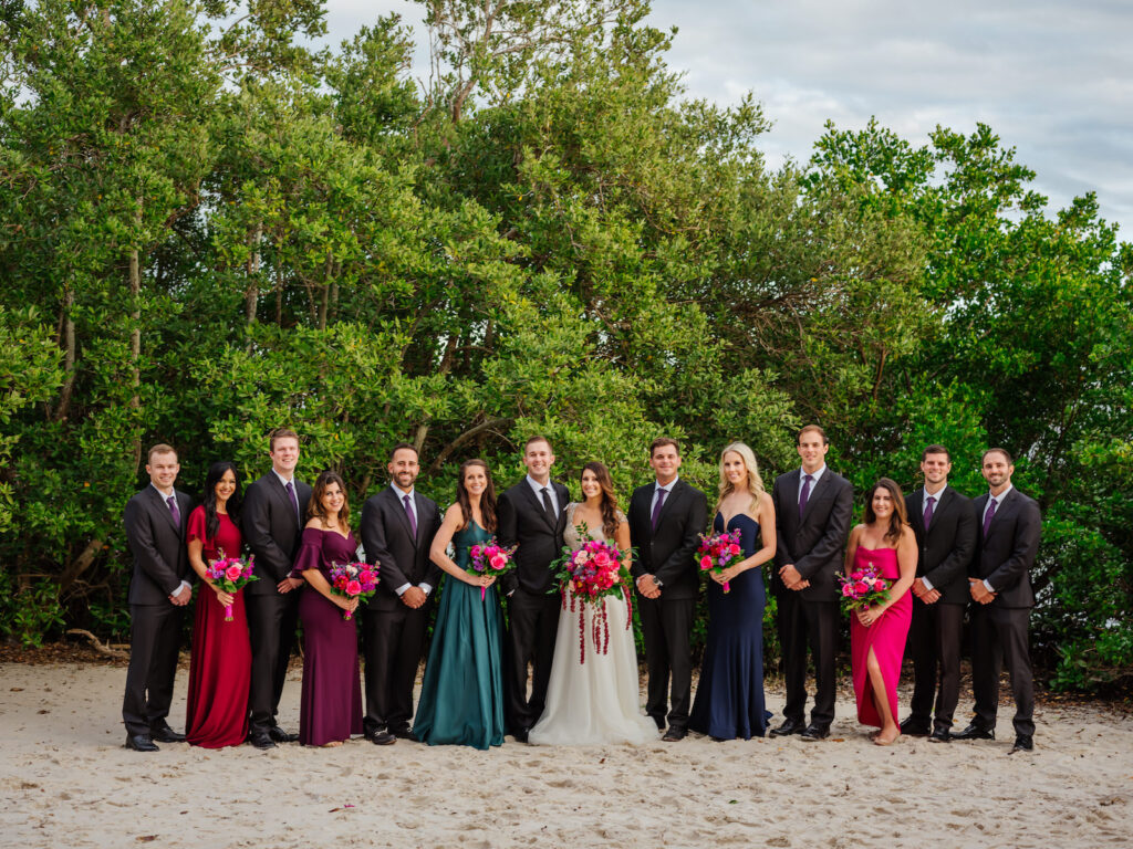 Florida Bride Holding Jewel Tone Floral Bouquet, Groom, Groomsmen, Bridesmaids in Mismatched Dresses Wedding Party Photo on Beach | Tampa Bay Wedding Florist Iza's Flowers | Wedding Planner Perfecting the Plan | Wedding Venue The Current Hotel Tampa