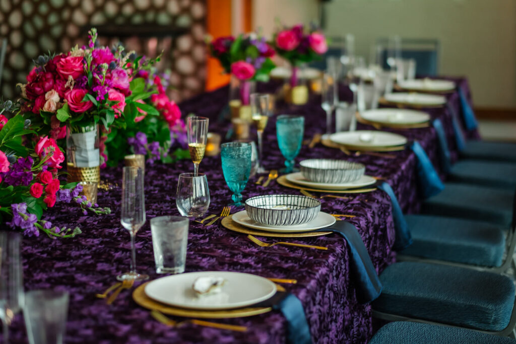 Jewel Tone Wedding Reception Decor, Long Table with Dark Purple Linen, Pink Roses, Greenery Low Floral Centerpiece, Gold Chargers, Blue Linen Napkins | Tampa Bay Wedding Planner Perfecting the Plan | Wedding Florist Iza's Flowers