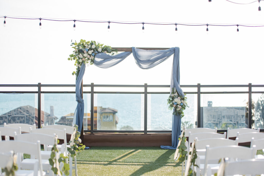 St. Pete Beach Rooftop Wedding Ceremony with White Chairs and a Wooden Arch with Blue Drapery | Wedding Venue Hotel Zamora | Tampa Bay Wedding Planner Elegant Affairs by Design
