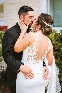 Florida bride wearing floral lace and illusion open back wedding dress hair updo with floral crystal hair piece kissing groom during first look | Tampa wedding photographer Bonnie Newman Creative | Wedding hair and makeup Femme Akoi