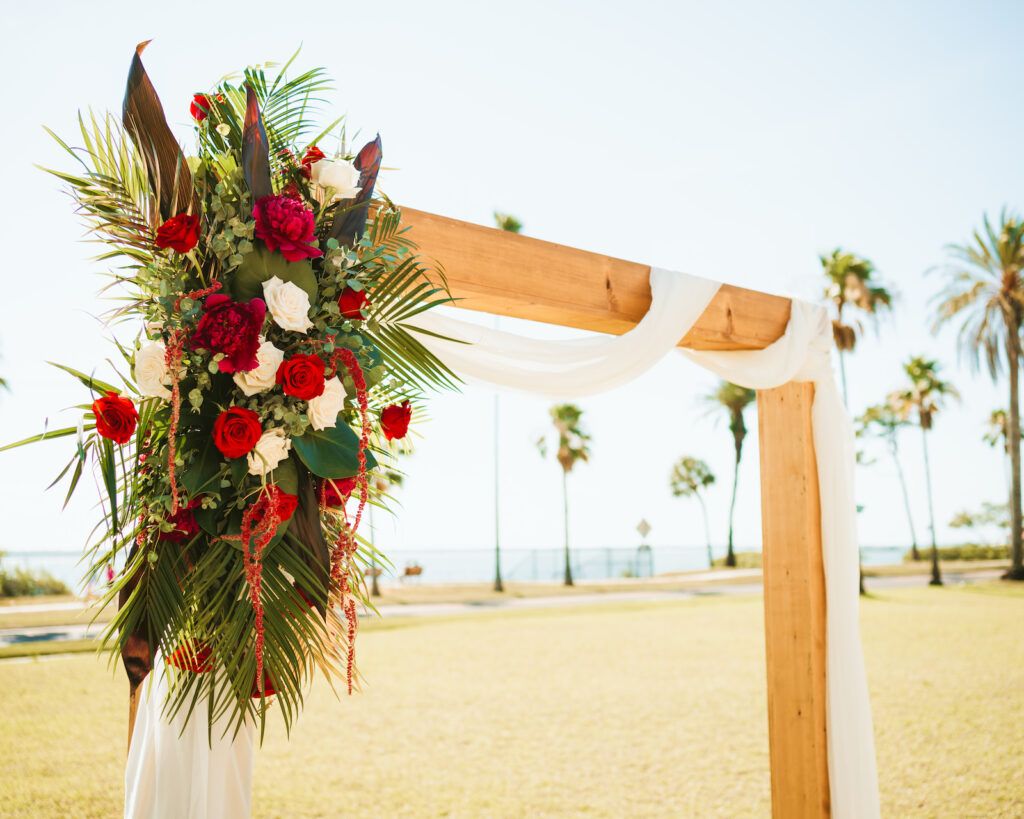 Fall wedding decor, wooden rectangular arch with white linen, red and white roses, hanging amaranthus, palm fronds and greenery floral arrangement | Tampa bay wedding photographer Bonnie Newman Creative | Wedding planner Coastal Coordinating | Wedding Florist Iza’s Flowners