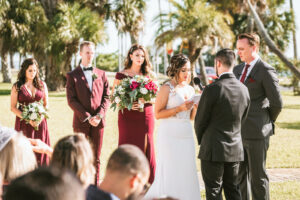Florida bride and groom exchanging wedding vows during ceremony, bridesmaids wearing burgundy red dresses, groomsmen wearing burgundy red suit | Tampa Bay wedding photographer Bonnie Newman Creative