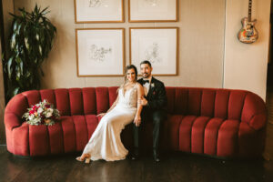 Classic bride and groom sitting on red velvet tufted couch wedding portrait | Tampa Bay wedding photographer Bonnie Newman Creative | Dunedin Wedding Venue Fenway Hotel