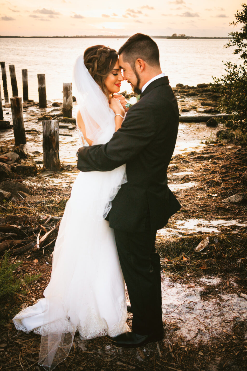 Florida bride with braided hair do, veil, red lipstick and groom waterfront wedding portrait | Tampa Bay wedding photographer Bonnie Newman Creative | Wedding hair and makeup Femme Akoi