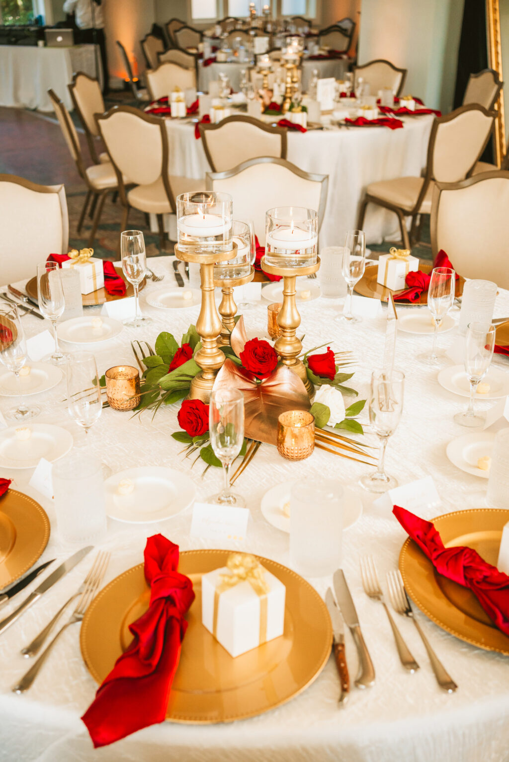 Fall classic wedding reception decor, gold chargers with red linen napkins, wedding favor box, gold candlestick floating candles centerpiece, red roses, palm fronds | Tampa Bay wedding photographer Bonnie Newman Creative | Wedding planner Coastal Coordinating | Wedding florist Iza’s Flowers