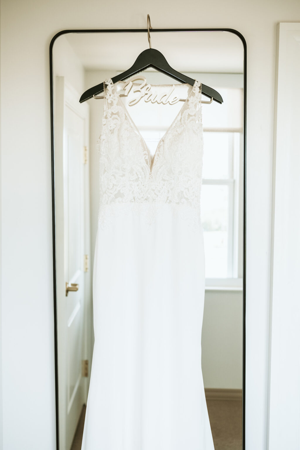 Classic fitted wedding dress with lace and illusion bodice hanging on mirror