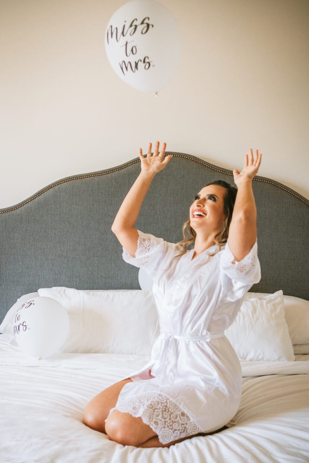 Florida bride on hotel bed getting wedding ready in lace trim white robe playing with miss to mrs balloon | Tampa wedding photographer Bonnie Newman Creative | Wedding hair and makeup Femme Akoi Beauty