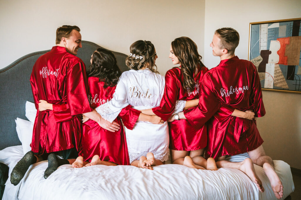 Florida bride, bridesmaids, and brides man in matching personalized red silk robes on bed | Tampa Bay wedding photographer Bonnie Newman Creative | Wedding hair and makeup Femme Akoi