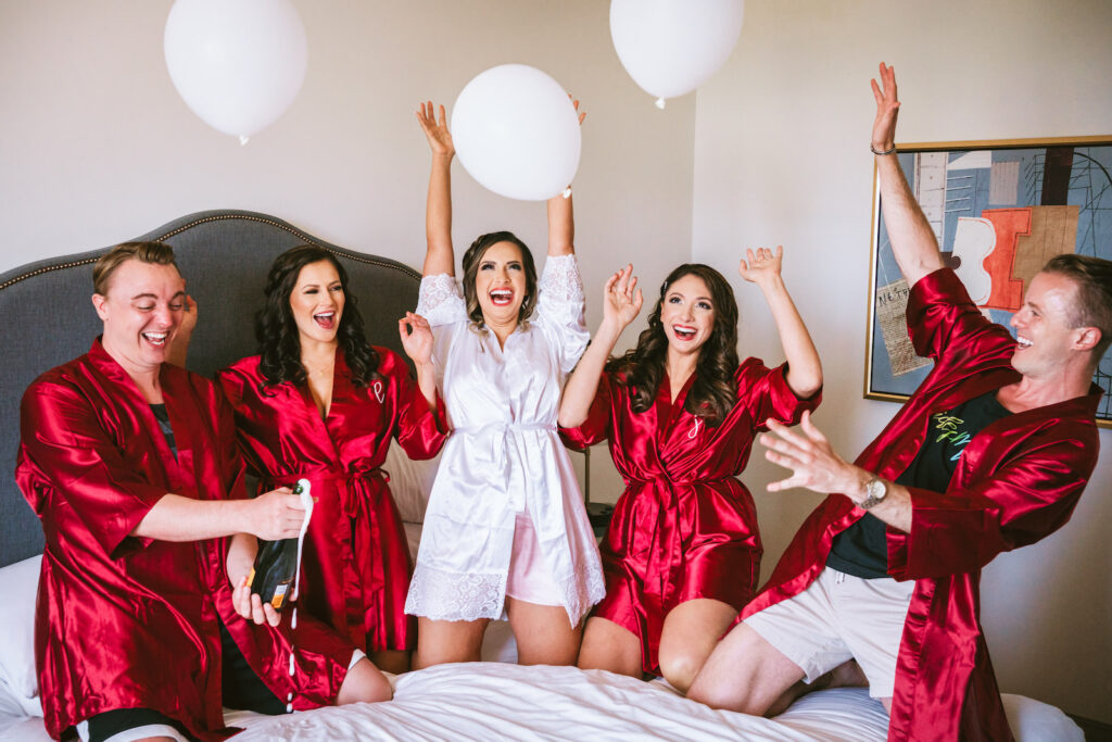 Florida bride, bridesmaids, and brides man in matching personalized red silk robes on bed | Tampa Bay wedding photographer Bonnie Newman Creative | Wedding hair and makeup Femme Akoi