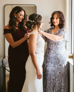 Florida bride getting wedding ready with mom and bridesmaid helping put dress on | Tampa wedding photographer Bonnie Newman Creative | Wedding hair and makeup Femme Akoi
