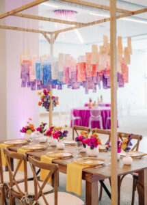 Whimsical Art Inspired Colorful Wedding Reception Decor, Wooden Feasting Table with Wooden Crossback Chairs, Yellow Linen Napkins, Low Pink, Yellow, Purple Floral Centerpieces, Hanging Watercolor Papers in Blue, Purple, Pink | Tampa Bay Wedding Planner Wilder Mind Events | Wedding Photographer Dewitt for Love | Wedding Rentals Gabro Event Services | Wedding Linens Over the Top Rental Linens | St. Pete Wedding Venue The James Museum
