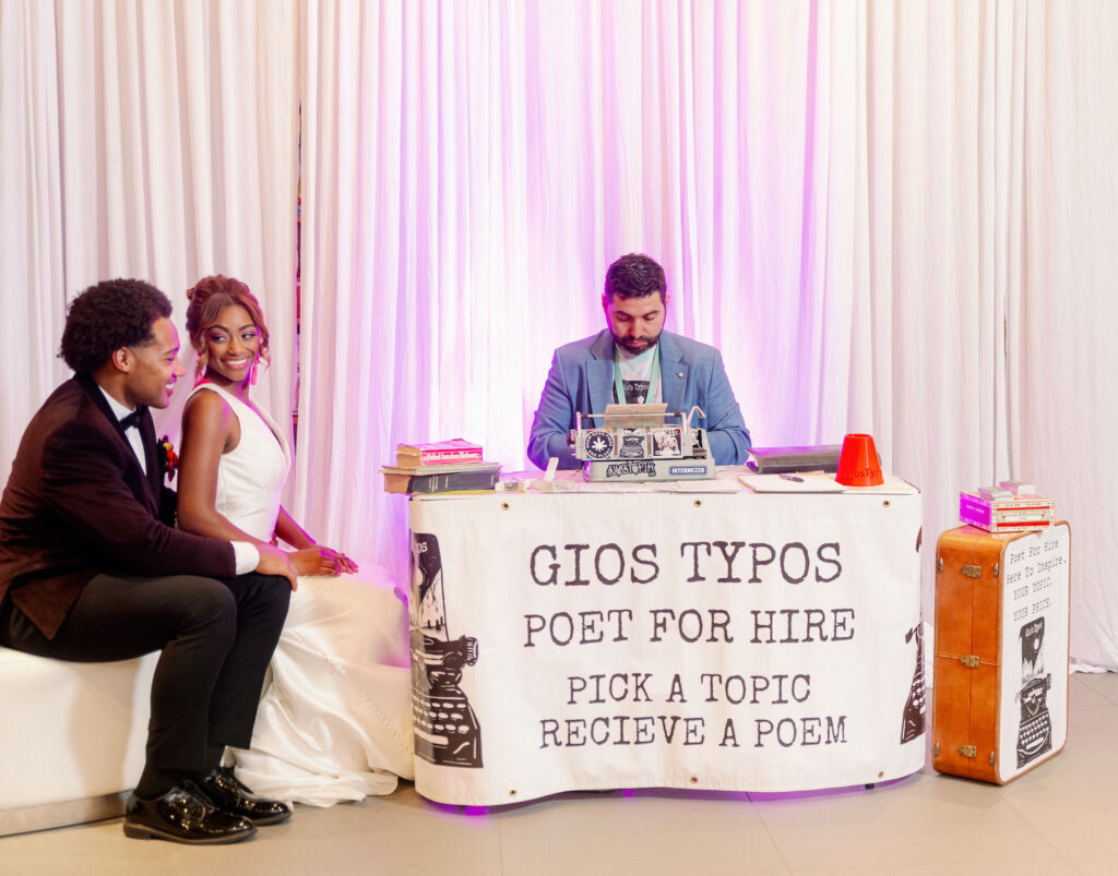 Bride and Groom at Whimsical Art Inspired Wedding Reception, Poet Typing on Typewriter, Purple Uplighting and White Linen Draping Backdrop | Tampa Bay Wedding Photographer Dewitt for Love | Wedding Planner Wilder Mind Events | Wedding Linens Over the Top Rental Linens