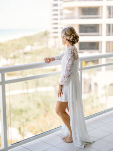 Florida Bride Getting Ready Overlooking Balcony of Gulf of Mexico, Wearing Silk White Robe with Floral Lace Sleeves | Sarasota Wedding Venue The Resort at Longboat Key Club