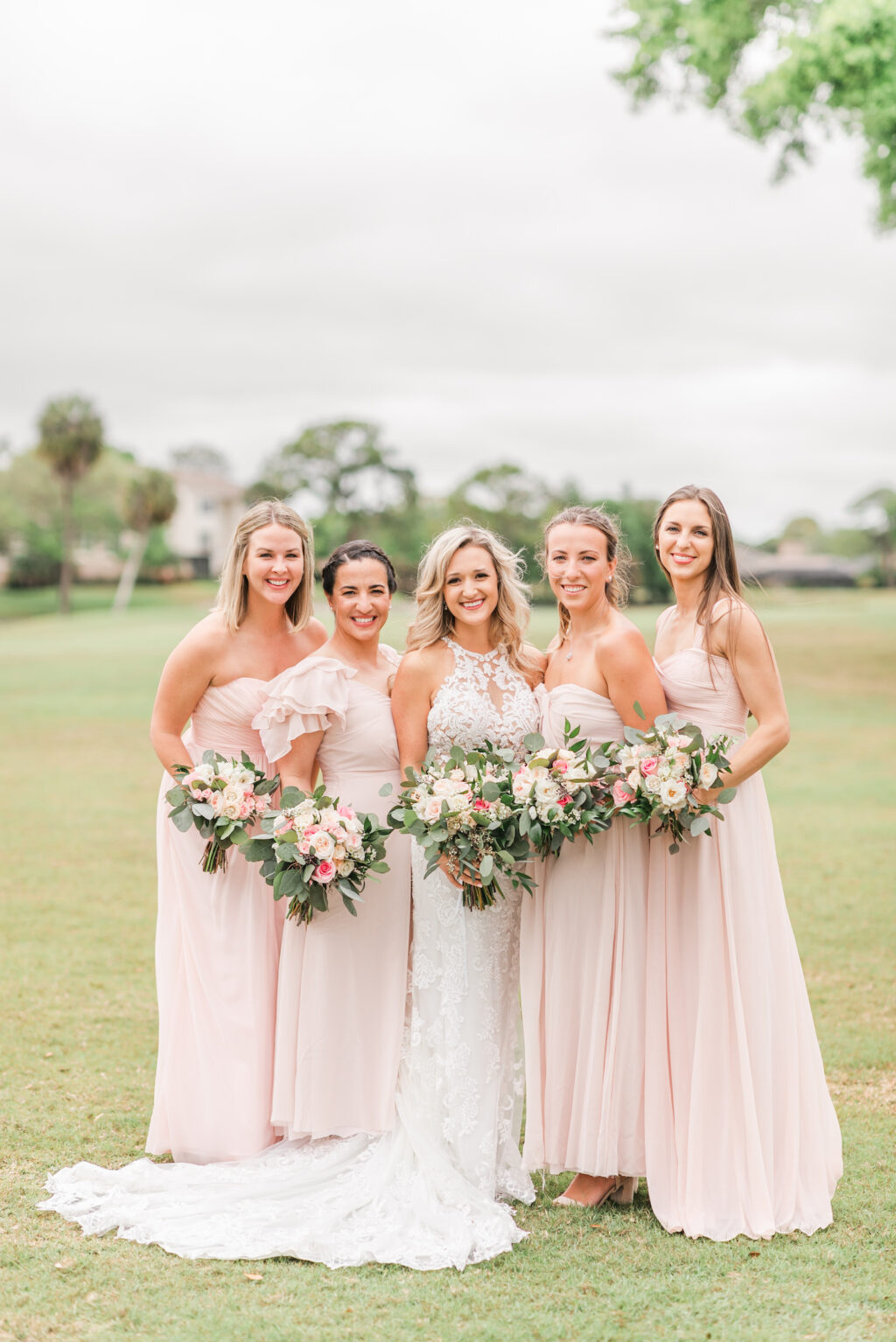 Romantic Pink St. Pete Garden Wedding | Bride Wearing Halter Lace Applique and Illusion Wedding Dress, Bridesmaids in Blush Pink Mix and Match Dresses Holding Floral Bouquets | Tampa Bay Wedding Florist Brides N Blooms Designs