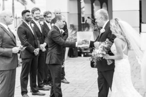 Romantic Pink St. Pete Garden Wedding Ceremony | Bride Walking Down the Aisle with Father Fist Bumping Groom Black and White Photo | Tampa Bay Wedding Florist Brides N Blooms Designs