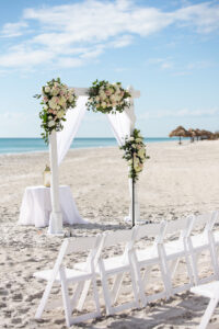White Wooden Arch with White and Blush Rose Floral Details with Greenery and White Drapery | Beachfront Wedding Ceremony The Resort at Longboat Key Club