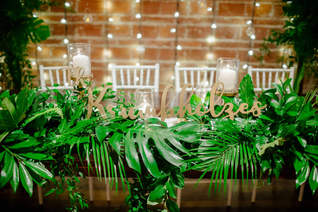 Tropical Inspired Florida Wedding Reception Decor, Greenery and Plant Leaf Flora Arrangements with Laser Cut Engraved Wooden Sign of Last Name at Head Table