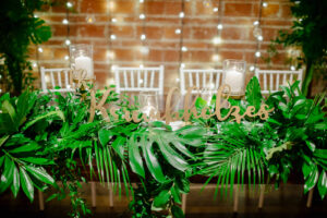 Tropical Inspired Florida Wedding Reception Decor, Greenery and Plant Leaf Flora Arrangements with Laser Cut Engraved Wooden Sign of Last Name at Head Table