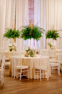 Tropical Elegant Wedding Reception and Decor, Round Tables with Champagne Linens and Tall Centerpieces with Greenery and Palm Leafs, White Chiavari Chairs, Gold Candle Sticks and Pineapples | Florida Wedding Venue NOVA 535
