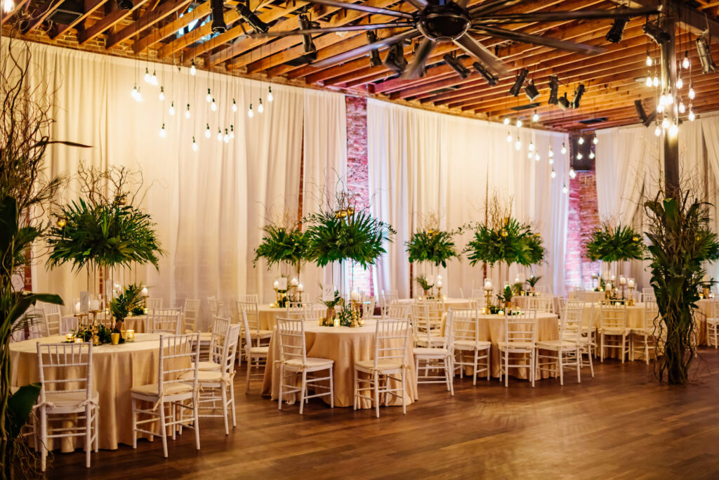 Tropical Elegant Wedding Reception and Decor, Round Tables with Champagne Linens and Tall Centerpieces with Greenery and Palm Leafs, White Chiavari Chairs, Gold Candle Sticks and Pineapples | Florida Wedding Venue NOVA 535 in Downtown St. Pete