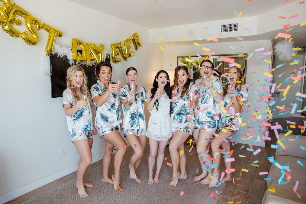 Florida Bride and Bridesmaids Popping Champagne and Throwing Confetti, Getting Ready, Bridal Party Wearing Matching Silk Pajamas, Pale Pink with Tropical Palm Leaf Print