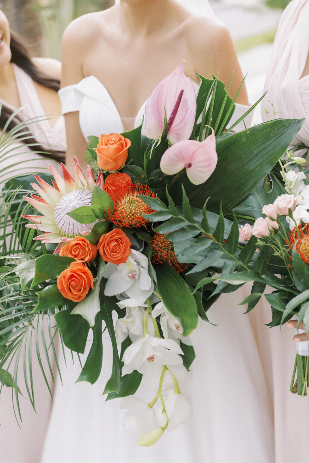 Bride holding Tropical Floral Bouquet, King Protea, Coral Orange Roses, Orange Pin Cushion Protea, Monstera and Palm Fronds, Hanging White Orchids, Pink Anthurium | Tampa Bay Wedding Planner Coastal Coordinating | Lemon Drops Floral