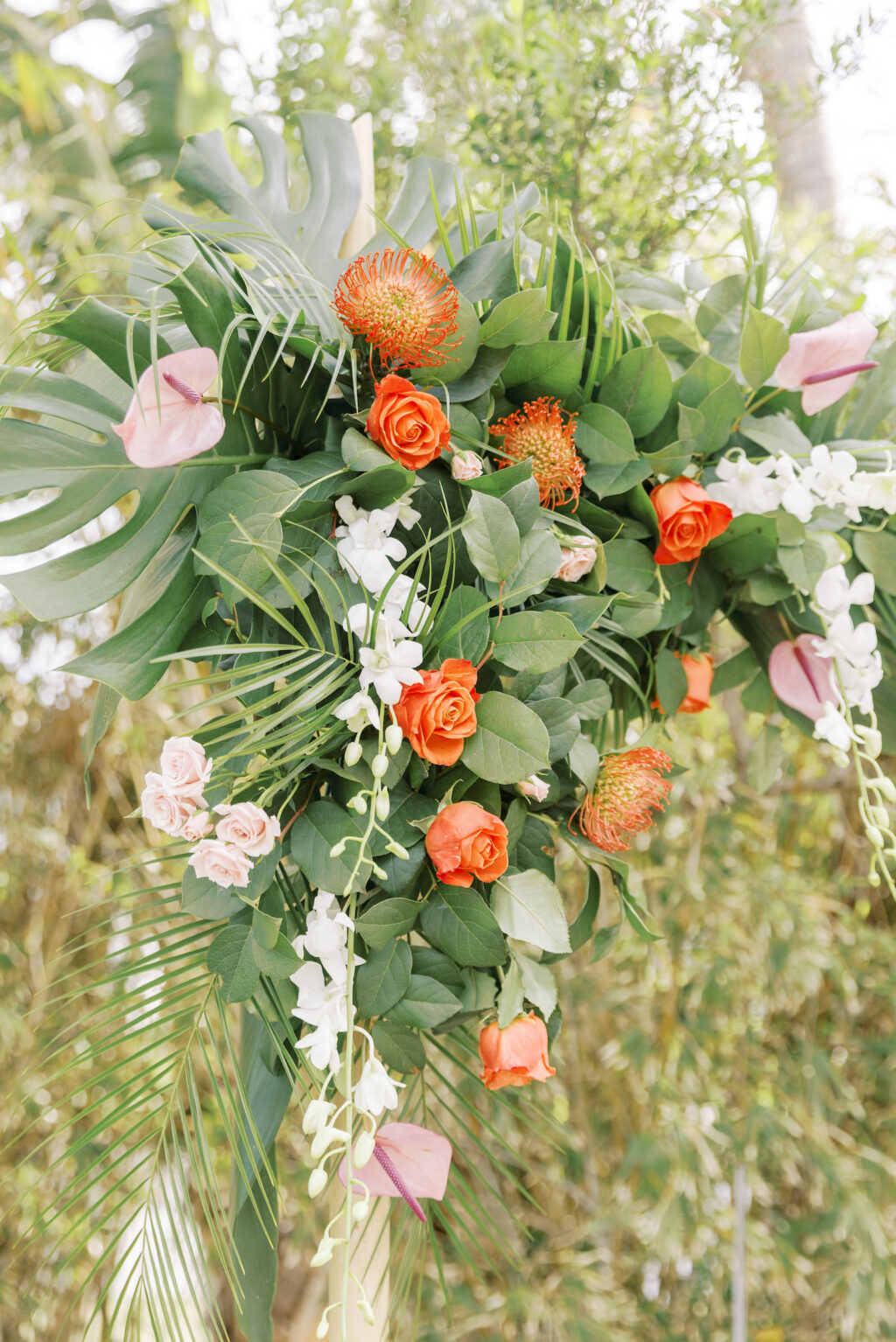 Tropical Pink and Green Wedding Ceremony Decor, Bamboo Arch with Monstera and Palm Fronds, Orange Roses, Pin Cushion Protea, Pink Anthurium, White Hanging Orchids | Tampa Bay Wedding Planner Coastal Coordinating