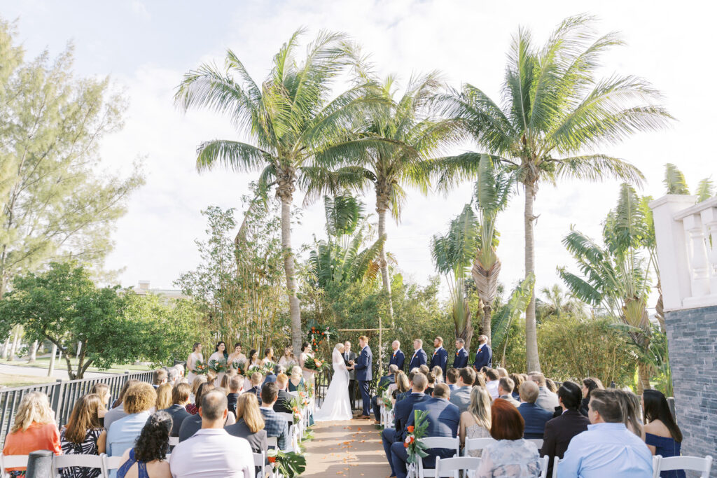 Tampa Bride and Groom Exchanging Wedding Vows | Tropical Pink and Green Outdoor Courtyard Wedding Ceremony Decor, Monstera Palm Leaves with Orange and Pink Flowers, Bamboo Arch | Tampa Bay Wedding Planner Coastal Coordinating | St. Pete Wedding Venue Hotel Zamora