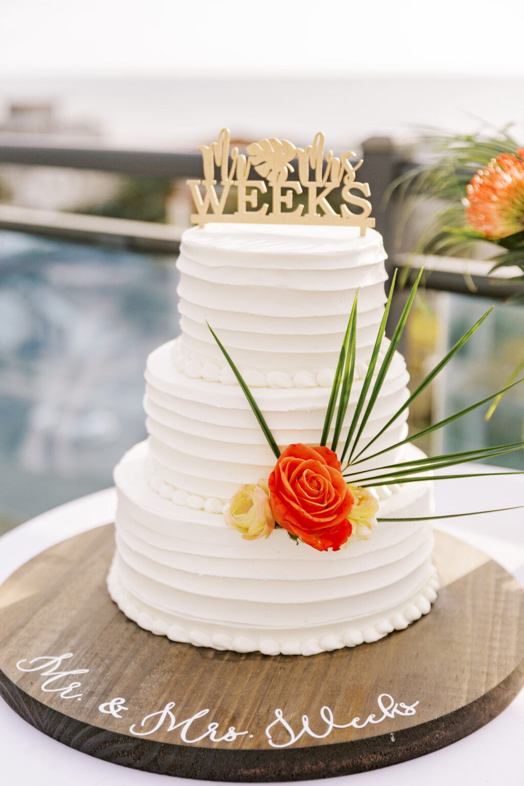 Three Tier Textured White Wedding Cake with Orange and Yellow Roses, Palm Fronds, Laser Cut Gold Cake Topper on Wooden Cake Stand | Tampa Bay Wedding Planner Coastal Coordinating