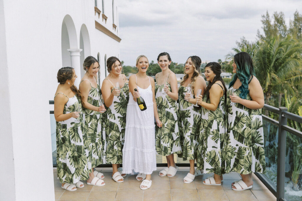 Tropical Pink and Green Wedding, Bridesmaids in Matching Palm Leaf Dresses, Bride Popping Bottle of Champagne, Balcony Photo | St. Pete Wedding Venue Hotel Zamora | Tampa Bay Wedding Hair and Makeup Savannah Olivia Beauty