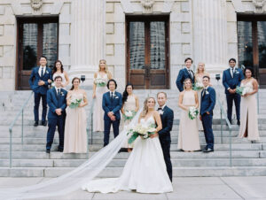 White and Green Modern Minimalist Tropical Wedding Party, Bridesmaids Wearing Mix and Match Champagne Dresses, Groomsmen in Navy Blue Suits, Bride Wearing Spaghetti Strap V Neckline Chic A-Line Wedding Dress and Full Length Veil Holding White Flowers and Palm Leaf Bouquet, Groom Wearing Navy Blue Tuxedo | Tampa Bay Wedding Hair and Makeup Femme Akoi Beauty Studio | Steps of Historic Courthouse Le Meridien
