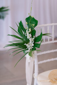 White and Green Modern Minimalist Tropical Wedding Ceremony Decor, White Chiavari Chairs with Palm Frond and Monstera Leaf with White Orchid Flower Arrangement | Tampa Bay Wedding Planner Taylored Affairs