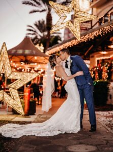 Bride and Groom Wearing Blue and Black Tuxedo Walking Outside St. Pete Wedding Venue The Birchwood with Christmas Light Decor