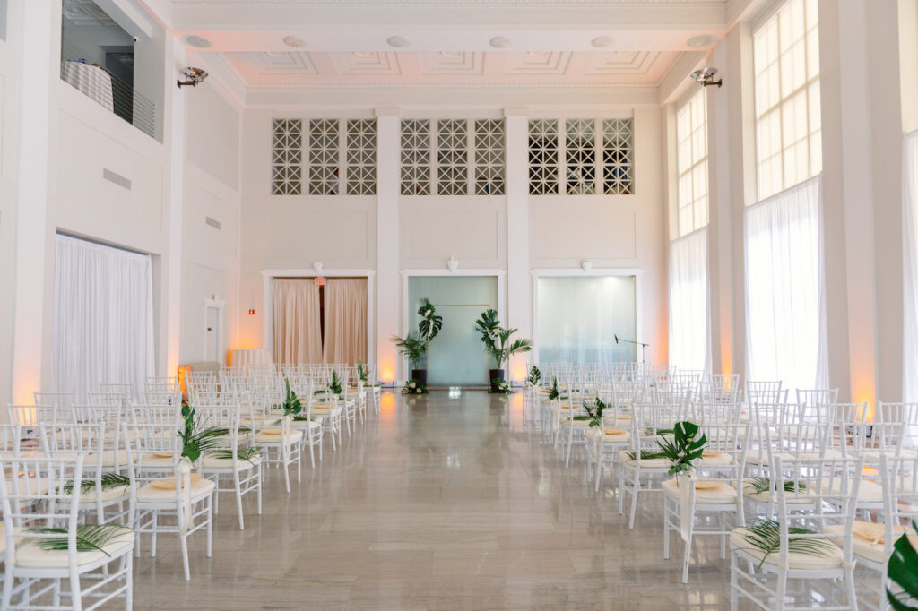 White and Green Modern Minimalist Tropical Wedding Ceremony Decor, White Chiavari Chairs with Palm Leaf Floral Arrangements, Monstera Leaves and Palm Fronds Planted Pots | Tampa Bay Wedding Planner Taylored Affairs | Downtown Tampa Historic Wedding Venue The Vault